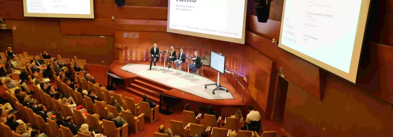 Personas asistiendo a una charla empresarial en un auditorio con panelistas en el escenario.