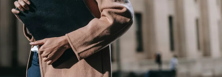 Persona sosteniendo una carpeta negra frente a un edificio difuminado.