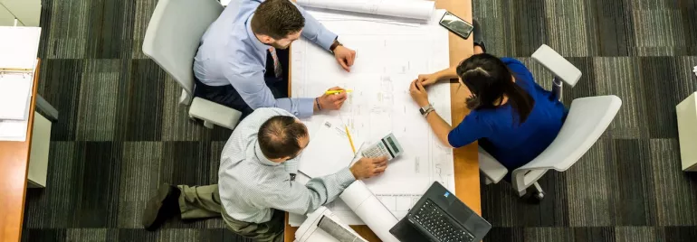 Tres personas revisan planos en una sala de reuniones.
