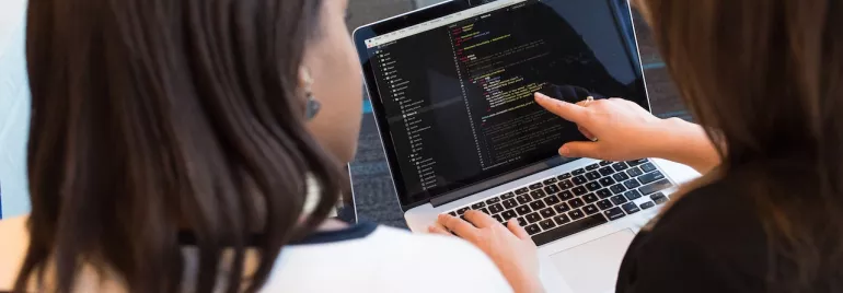 Dos personas revisan código en una computadora portátil.