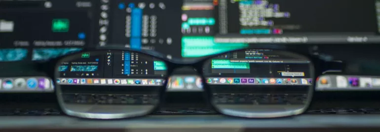 Gafas frente a una pantalla con código y gráficos de computadora.
