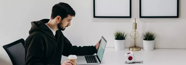 Persona trabajando en una computadora portátil mientras sostiene una taza de café en una oficina moderna.