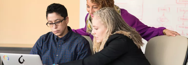 Tres personas colaborando frente a una computadora portátil.