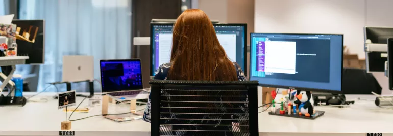 Persona trabajando en escritorio con múltiples monitores y una laptop.