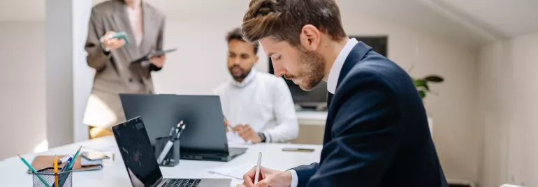 Personas trabajando en una oficina con portátiles y papeles.