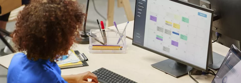 Persona trabajando en un escritorio con una computadora mostrando un calendario.