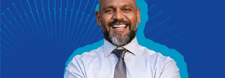Persona sonriente con camisa clara y corbata en fondo azul.