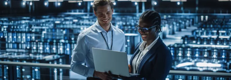 Dos personas miran una computadora portátil en un centro de datos iluminado.