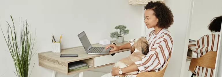 Persona trabajando en computadora portátil con un perro en brazos.