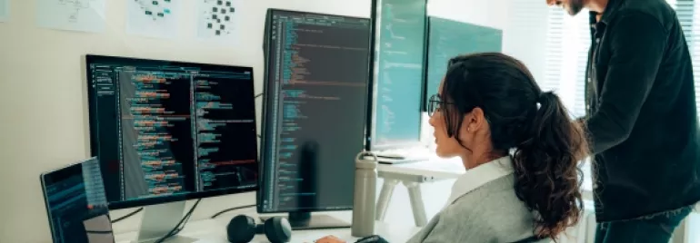 Personas trabajando en programación con varios monitores en una oficina.