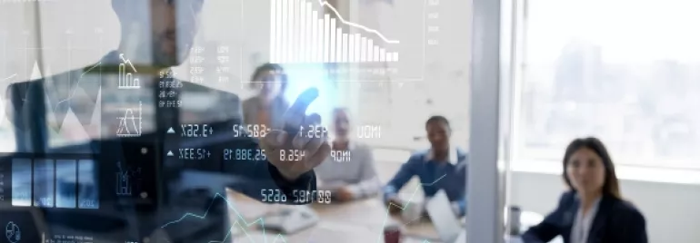 Hombre presentando datos gráficos en una pantalla transparente en una sala de reuniones.