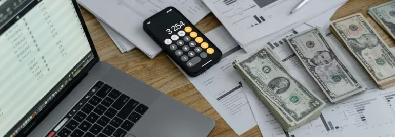 Imagen de una mesa con notas, ordenador, calculadora y billetes