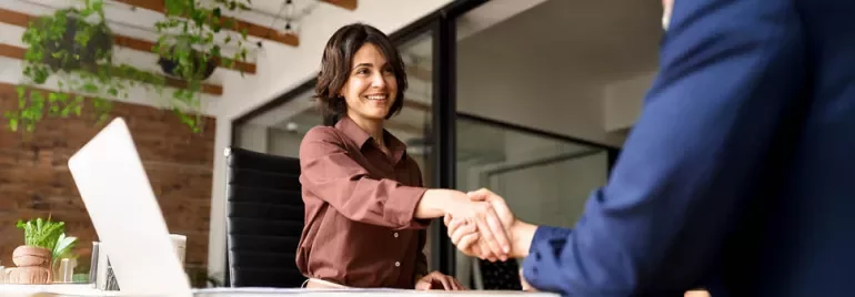 Mujer dándole la mano de forma profesional a un hombre sentados como en entrevista