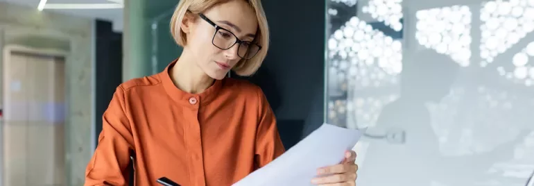 Mujer rubia con gafas leyendo un documento.