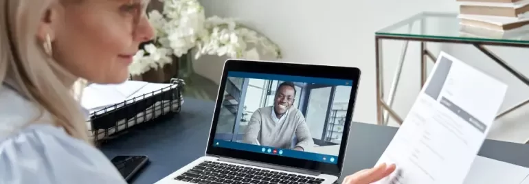 Mujer haciendo una entrevista de trabajo online mirando el CV del candidato que aparece en la pantalla de su ordenador