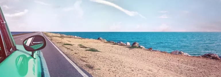 Un coche verde en una carretera junto al mar.