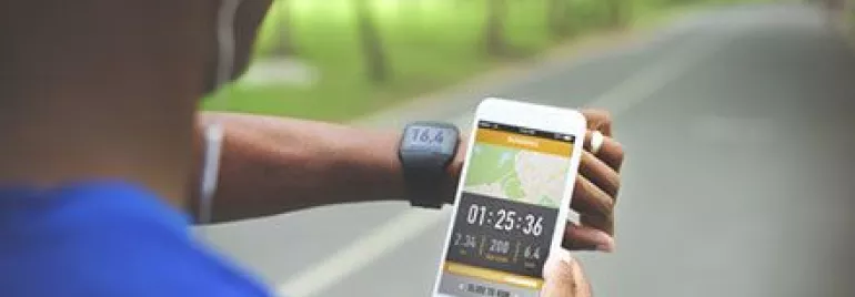 Persona usando una aplicación de ejercicio en el teléfono y un reloj inteligente en un camino.