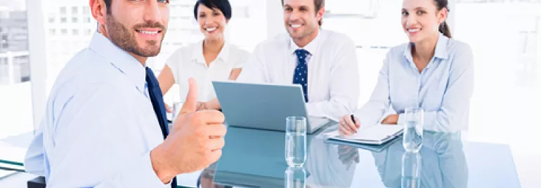 Un grupo de personas en una reunión de negocios, con una persona mostrando un pulgar arriba.