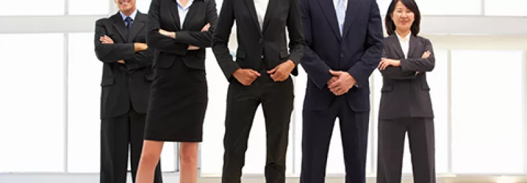 Un grupo de profesionales en traje sonríe en una oficina luminosa.