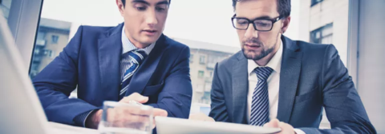 Dos personas en trajes revisan un documento en una oficina.