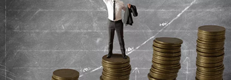 Hombre levantando los brazos sobre una pila de monedas en un gráfico ascendente.