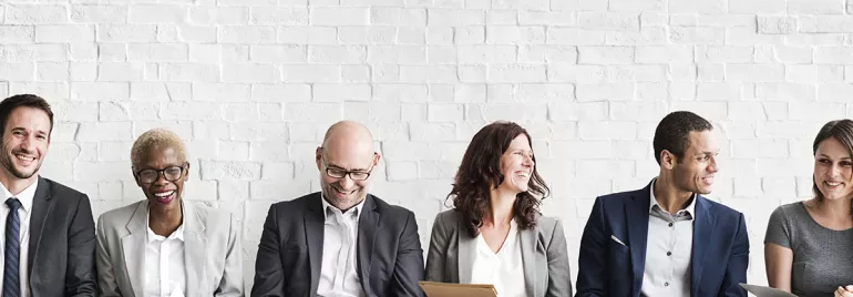 Personas sentadas contra un muro blanco, algunas sonriendo.