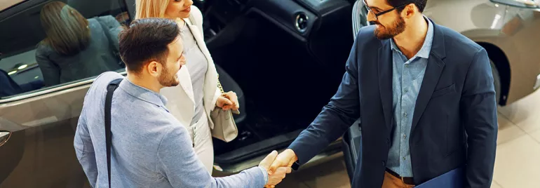 Personas estrechando manos en un concesionario de coches.