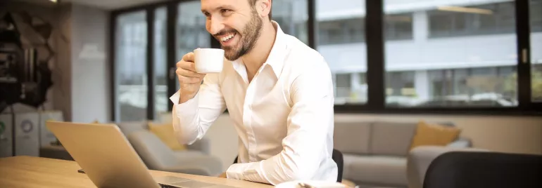 Persona sonriente bebiendo café frente a un portátil.