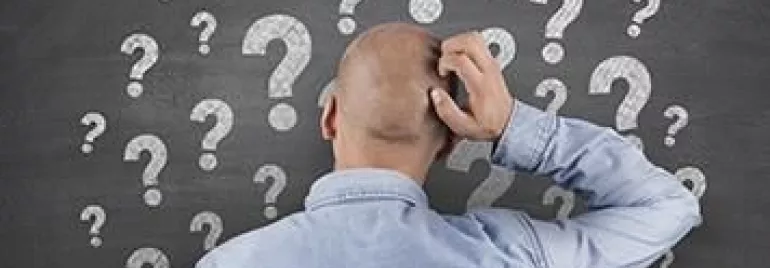 Persona rascándose la cabeza frente a una pizarra con signos de interrogación.