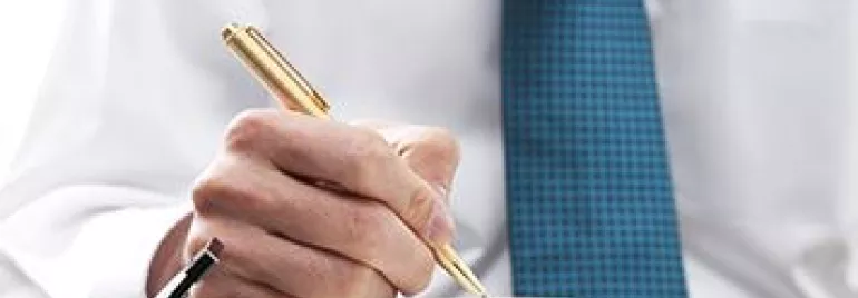 Persona usando una pluma dorada para escribir en una agenda.