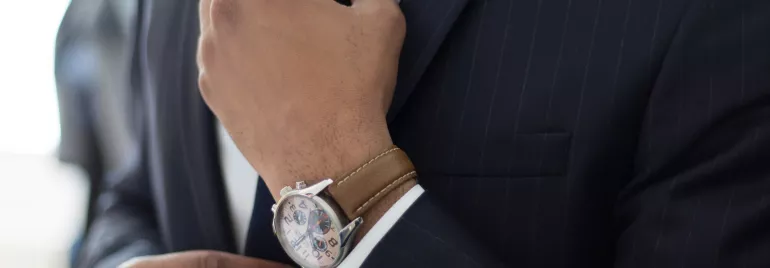 Persona ajustando una corbata y llevando reloj mientras lleva un traje.