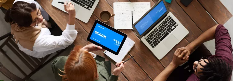 Reunión de grupo alrededor de una mesa con portátiles y tablets.