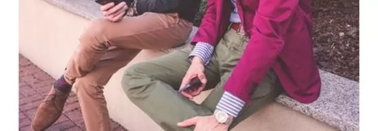 Dos personas sentadas en un banco usando teléfonos móviles.