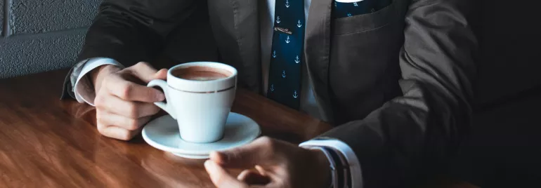 Persona en traje bebiendo café en una mesa de madera.