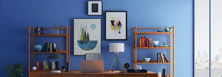 Una oficina con escritorio de madera y estantes llenos de libros, contra una pared azul con arte.