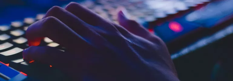 Mano sobre teclado iluminado por luces azules.