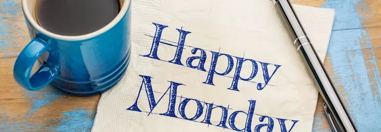 Taza de café y bolígrafo al lado de servilleta que dice 'Happy Monday'.