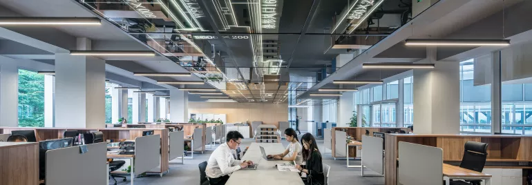 Oficina moderna con personas trabajando en una mesa central.