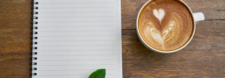 Taza de café con latte arte y cuaderno sobre mesa de madera