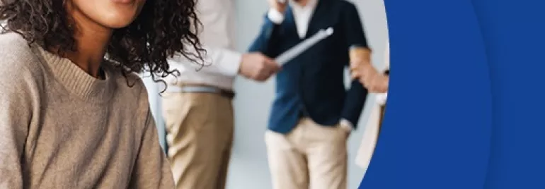 Persona sonriente sentada en una oficina mientras otros trabajan en segundo plano.