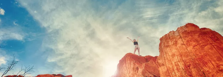 Persona en la cima de una montaña de roca roja bajo un cielo despejado.