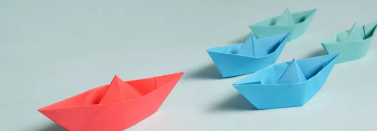 Botes de papel en fila, uno rojo y otros azules.