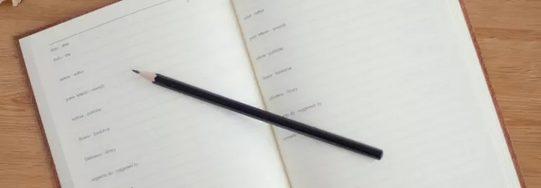 Un cuaderno abierto con un lápiz negro y una taza de café en una mesa de madera.