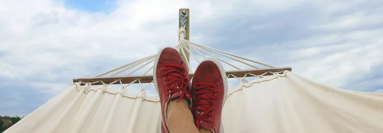 Relajación en una hamaca con zapatos rojos bajo el cielo azul.