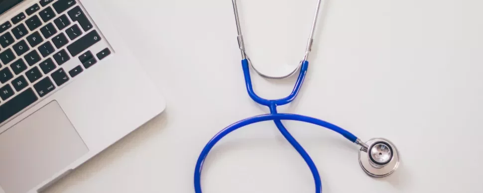Estetoscopio azul junto a una laptop en una mesa blanca.