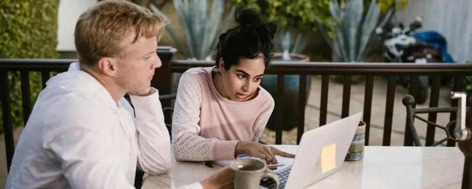 un chico y una chica mirando el ordenador mientras señalan algo en la pantalla