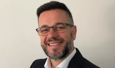 Hombre con barba y gafas sonriendo en traje, fondo blanco.