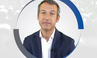 Persona de cabello oscuro con traje y corbata, frente a un fondo difuminado.
