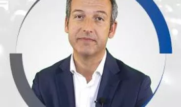 Retrato de una persona con traje oscuro y fondo neutro.