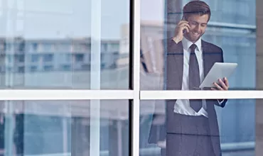 Persona en traje usando tablet y teléfono detrás de una ventana en un edificio.